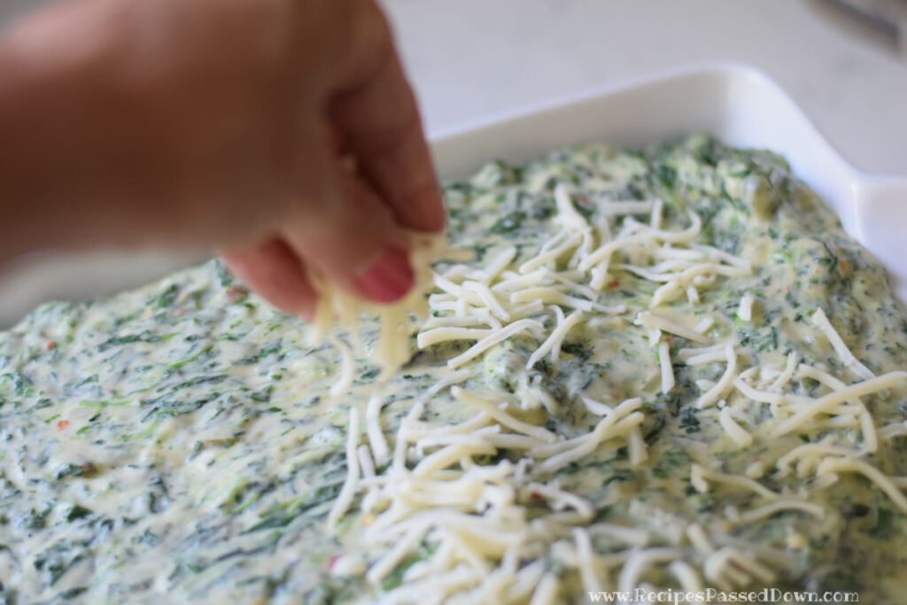 sprinkling cheese onto spinach maria in baking pan